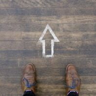 The way forward: A man standing in front of arrow sign on wooden floor